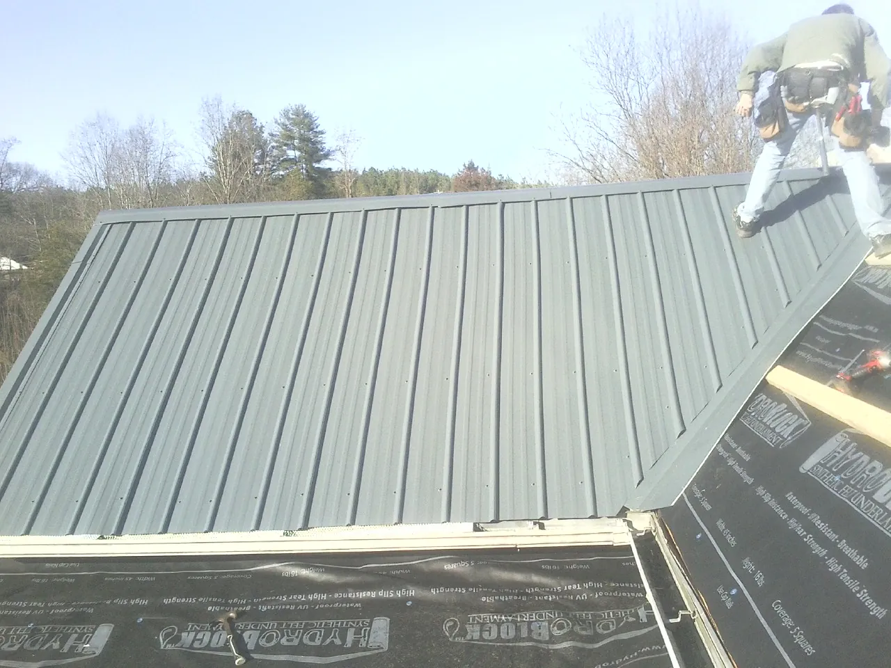 Crew installing dark green standing seam panels over synthetic underlayment in Economy