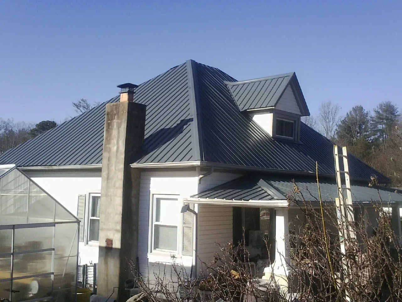 Dark blue standing seam metal roof on a white farmhouse with dormer — Slate & Tile Roof Repair by Roofing Brothers in Economy