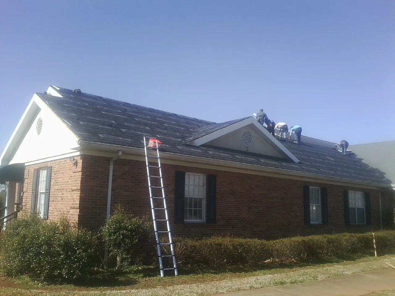 Crew tearing shingles off a brick ranch roof with a ladder set — Emergency Roof Repair work by our crew in Economy