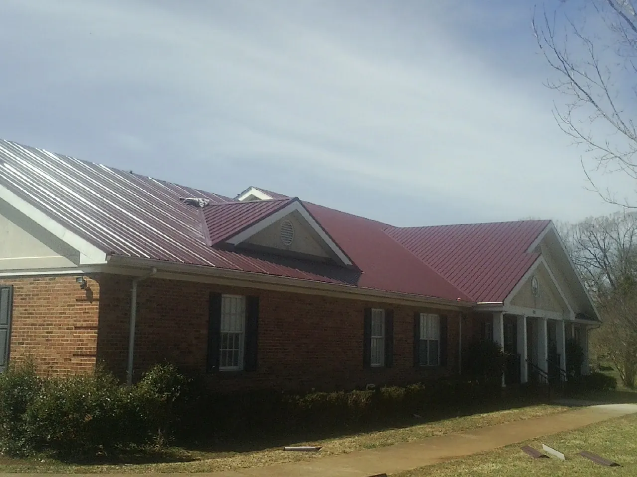 Red metal roof with gabled entries on a long brick building, from a Hail Damage Roof Repair job in Economy