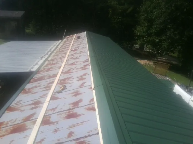 Old rusted panels beside newly installed green metal roofing — Wind Damage Roof Repair by Roofing Brothers in Economy