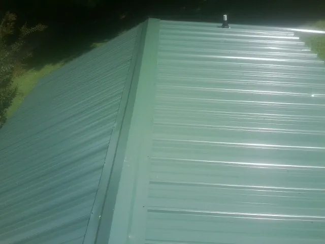 New green metal panels meeting at the ridge of a roof — Flat Roof Repair work by our crew in Economy