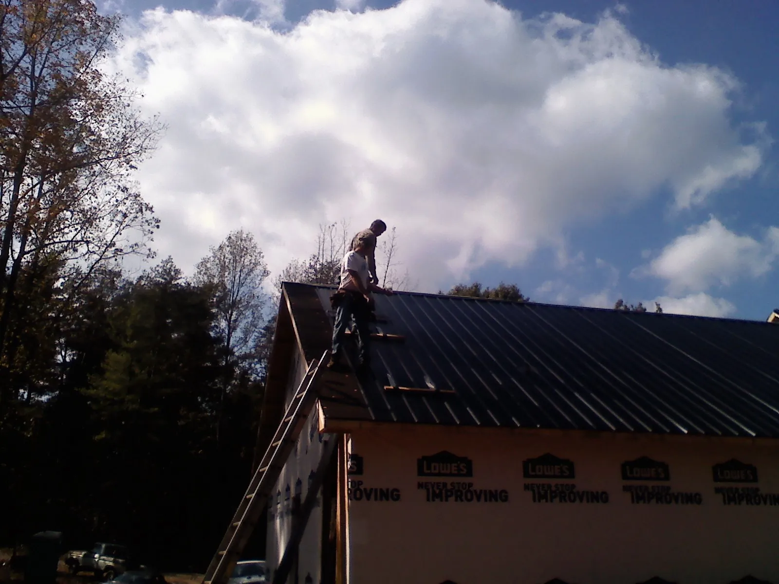 Roofer fastening dark metal panels high against a cloudy sky, from a Roof Inspection job in Economy