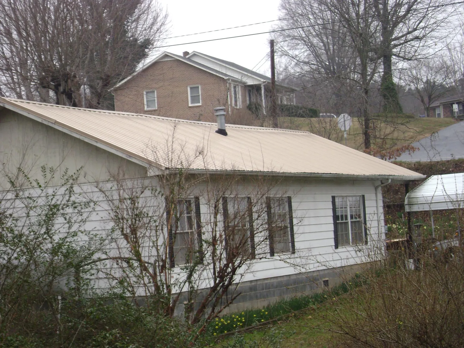 Tan metal roof on a white sided house set into a hillside — Commercial Roofing by Roofing Brothers in Economy