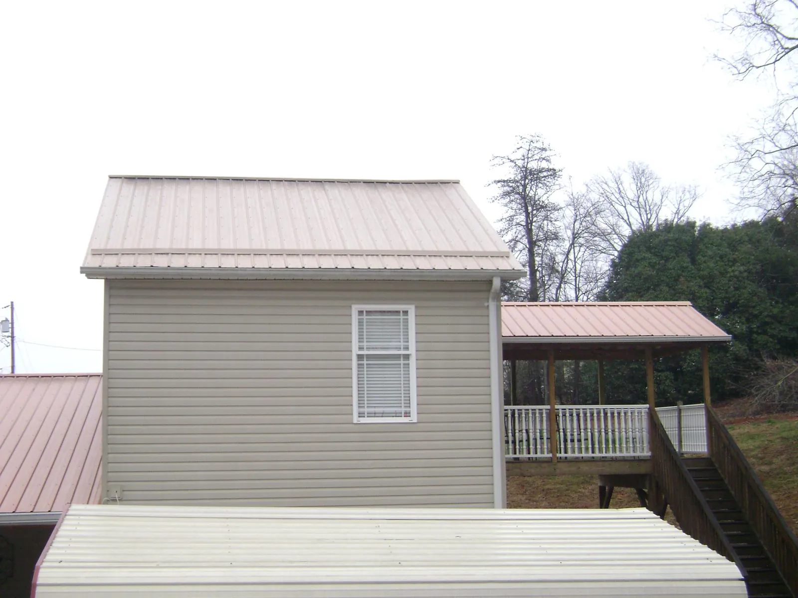 Tan metal roofs on a two story addition and attached porch, from a Roof Replacement job in Economy